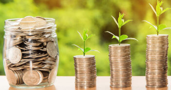 Jar of coins beside growing stacks of coins with seedlings sprouting from the top