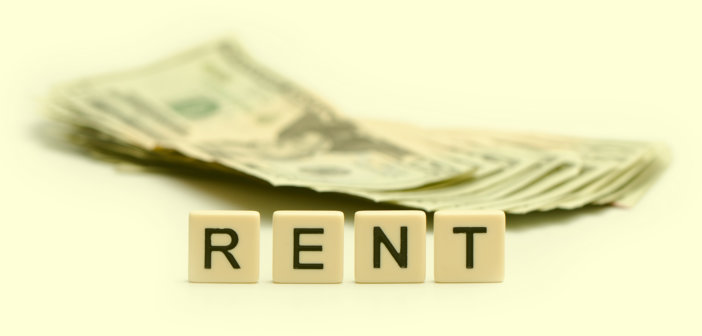 R E N T spelled out on tiles in front of a stack of cash