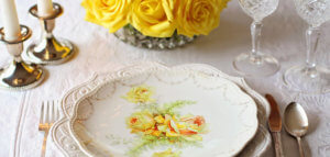 Fancy place setting of fine china_ polished silverware_ crystal goblets_ brass candlesticks and a vase of roses