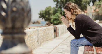 Person saying a prayer sitting on a bench
