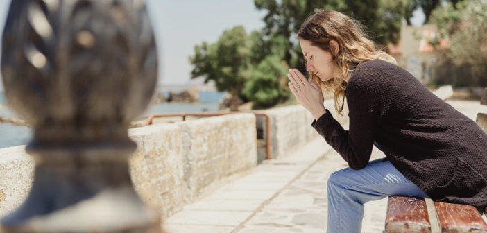 Person saying a prayer sitting on a bench