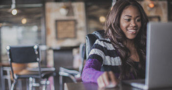 Smiling person using a laptop computer in a cafe