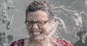 Grimacing person being pelted with large splashes of water