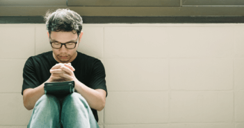 Person praying with bowed head and closed eyes in a corridor