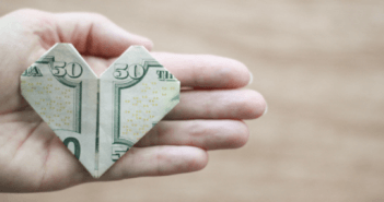 $50 bill folded into an origami heart in the open palm of a person's hand