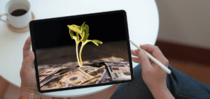 Person holding a tablet computer with a screen showing a plant seedling metaphorically growing from cash currency