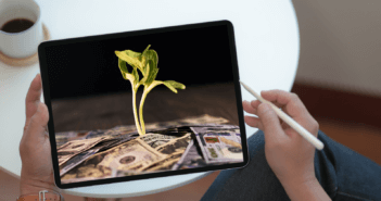 Person holding a tablet computer with a screen showing a plant seedling metaphorically growing from cash currency