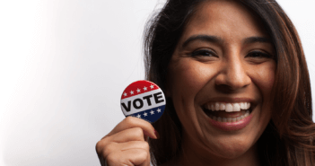 Smiling person holding a VOTE button