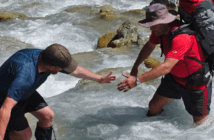 What Does Strong Leadership Look Like? Backpacker lending a hand to help another cross a stream