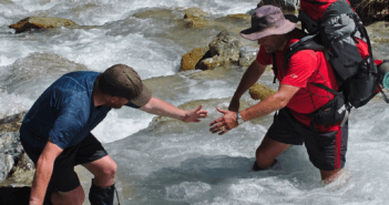 Backpacker lending a hand to help another cross a stream