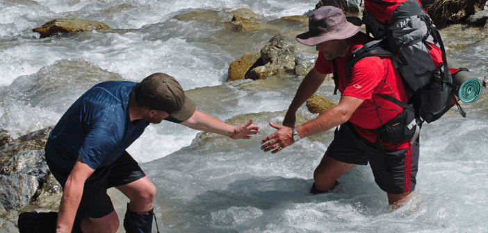 Backpacker lending a hand to help another cross a stream