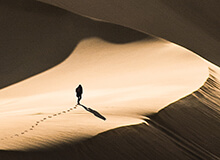 Lone person walking through vast desert sand dunes