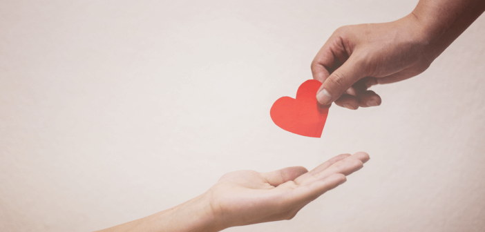 A person's hand placing a paper heart in the outstretched hand of another person