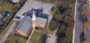 Bird's eye view of a church with a large empty parking lot beside a busy road