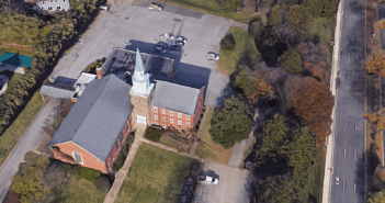 Bird's eye view of a church with a large empty parking lot beside a busy road