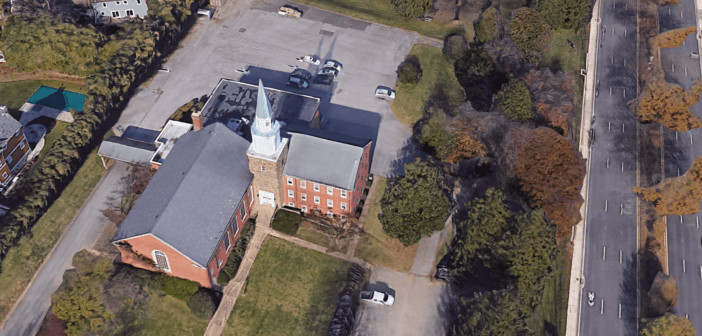 Bird's eye view of a church with a large empty parking lot beside a busy road