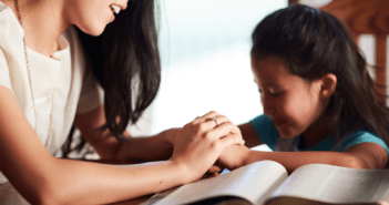 Parent and child at the dining table reading the Bible and praying together