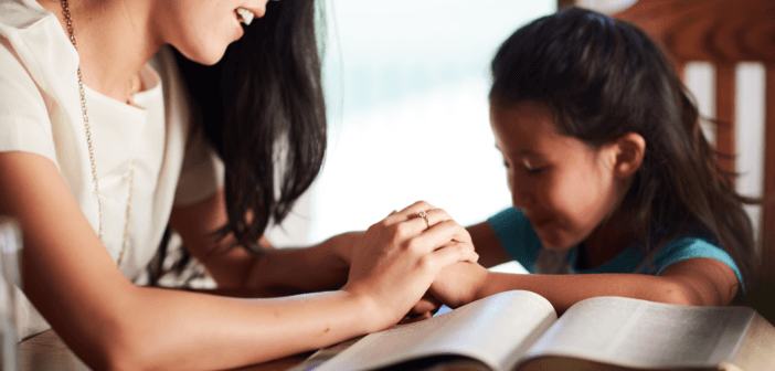 Parent and child at the dining table reading the Bible and praying together