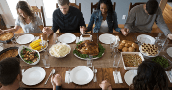 Holding hands and heads bowed in prayer around a Thanksgiving table