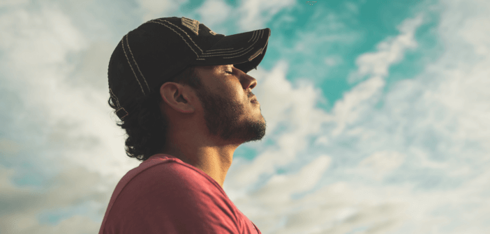 Person standing outside with eyes closed and face pointing toward the sky