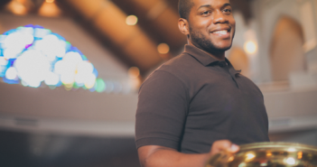 Smiling young adult holding an offering plate