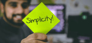 Person holding up a post-it note that reads SIMPLICITY