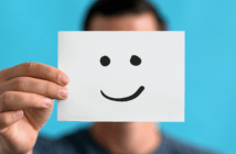 Person covering their face with a piece of paper with a drawn-on smiley face