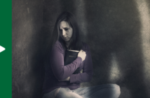 Abused person holding a Bible close to them while sitting alone in a dark corner, with a shadow of the abuser looming over