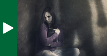 Abused person holding a Bible close to them while sitting alone in a dark corner, with a shadow of the abuser looming over