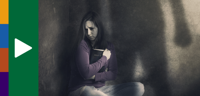 Abused person holding a Bible close to them while sitting alone in a dark corner, with a shadow of the abuser looming over