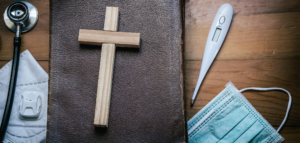 A Bible, small wooden cross, face mask, thermometer, and stethoscope