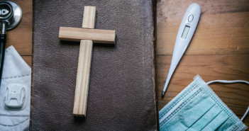 A Bible, small wooden cross, face mask, thermometer, and stethoscope