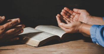 Two people praying over an open Bible