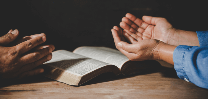 Two people praying over an open Bible