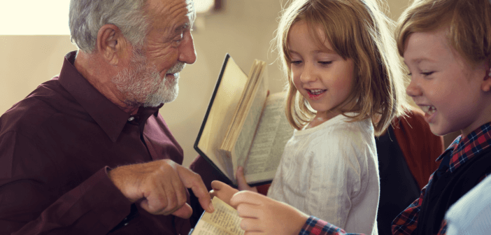 Older person pointing out a page in the Bible to two smiling young children