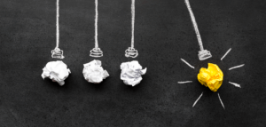 Wadded up paper representing light bulbs in a Newton's cradle. Three are white, and one is yellow, representing an idea. The yellow one is pulled back.