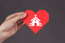 Hand holding a paper heart imprinted with a church building