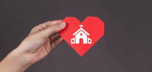 Hand holding a paper heart imprinted with a church building