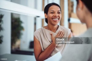 A woman smiles warmly with her hand on her chest, expressing