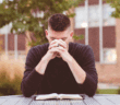 Young pastor sitting outside praying at a table with an open Bible on it
