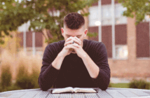 Young pastor sitting outside praying at a table with an open Bible on it