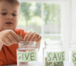 A child dropping coins into a glass jar labeled GIVE