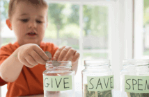 A child dropping coins into a glass jar labeled GIVE