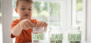 A child dropping coins into a glass jar labeled GIVE