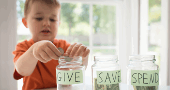 A child dropping coins into a glass jar labeled GIVE