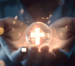Person holding in their hands a glass orb lit from within by a glowing cross
