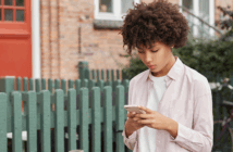 Reading the Cultural Signs Young adult looking down at their phone while walking down the sidewalk past a fence and house