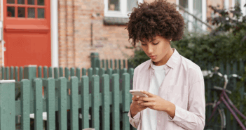 Reading the Cultural Signs Young adult looking down at their phone while walking down the sidewalk past a fence and house