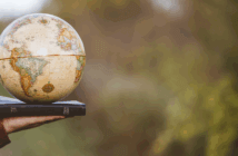 Photo of an outstretched hand holding a globe atop a Bible while in a country setting