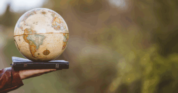 Photo of an outstretched hand holding a globe atop a Bible while in a country setting